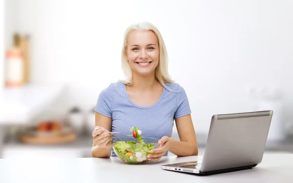 Smiling woman eating salad with laptop on kitchen Royalty Free Stock Photos