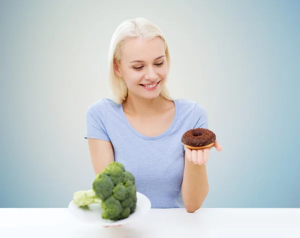 Smiling woman choosing between broccoli and donut Stock Image