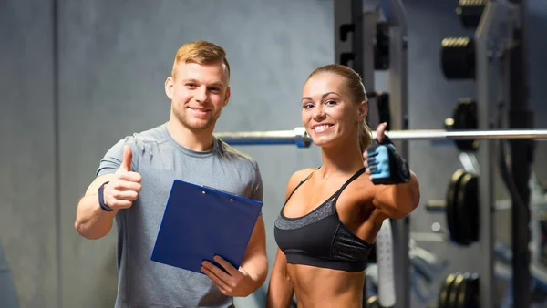 Leende ung kvinna med personlig tränare i gym — Stockfoto