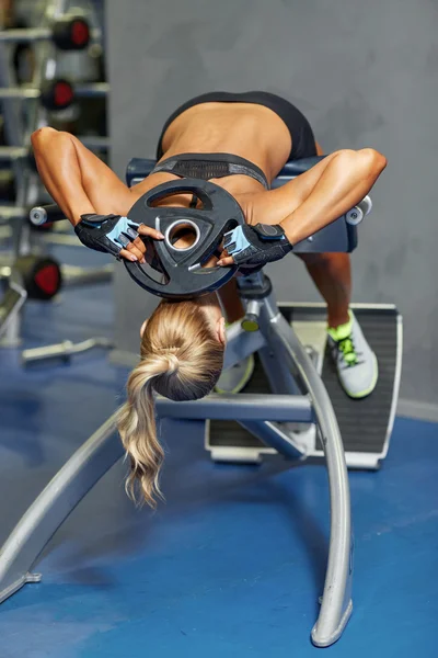 Mujer joven flexionando los músculos de la espalda en el banco en el gimnasio —  Fotos de Stock