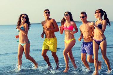 smiling friends in sunglasses running on beach clipart