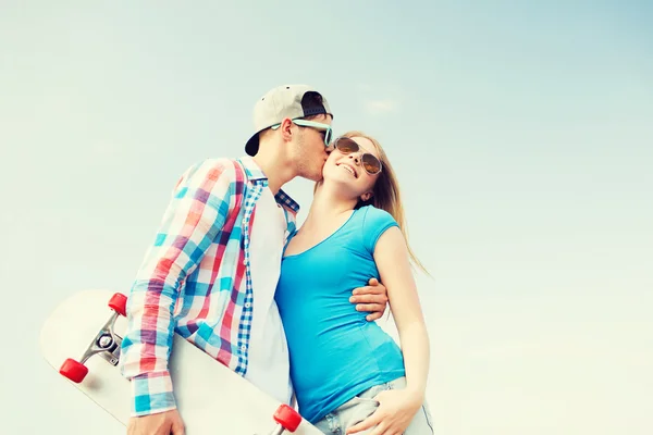 Улыбающаяся пара со скейтбордом целуется на открытом воздухе — стоковое фото