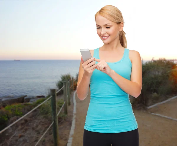 Glimlachend sportieve vrouw met smartphone outdoors — Stockfoto