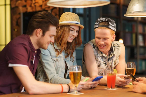 Счастливые друзья со смартфонами и напитками в баре — стоковое фото