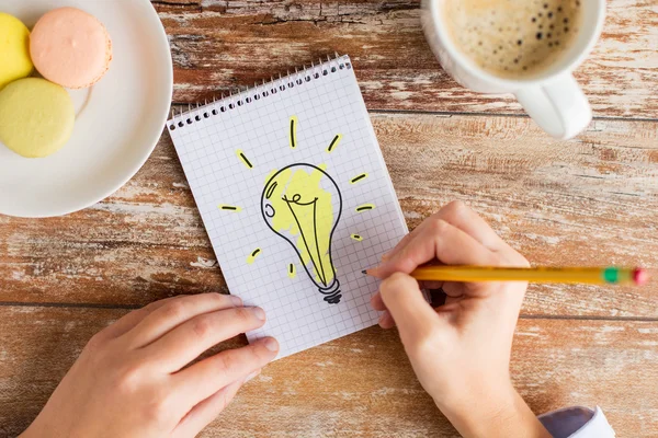 Primo piano di mani che disegnano la lampadina a notebook — Foto Stock