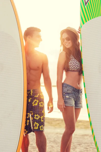 Casal sorridente em óculos de sol com surfes na praia — Fotografia de Stock