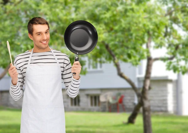 Happy man or cook in apron with pan and spoon — Stock Photo, Image