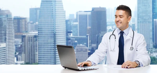 Усміхнений чоловік лікар з ноутбуком сидить за столом — стокове фото