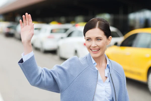 Leende ung kvinna med viftande hand över taxi — Stockfoto