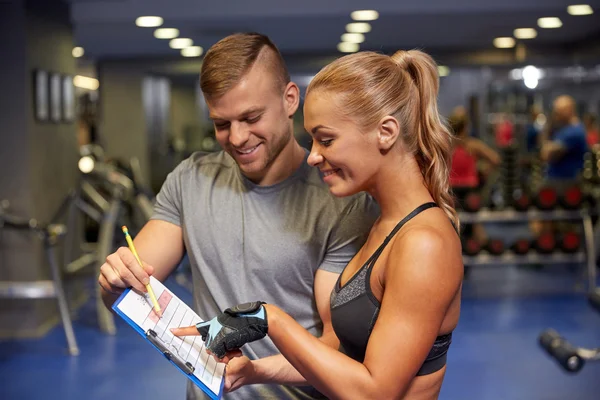 Wanita tersenyum dengan pelatih dan papan klip di gym — Stok Foto