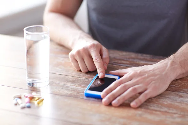 Close up of hands with smartphone, pills and water — Stock Photo, Image