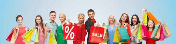 Happy people with sale sign on shopping bags — Stock Photo, Image