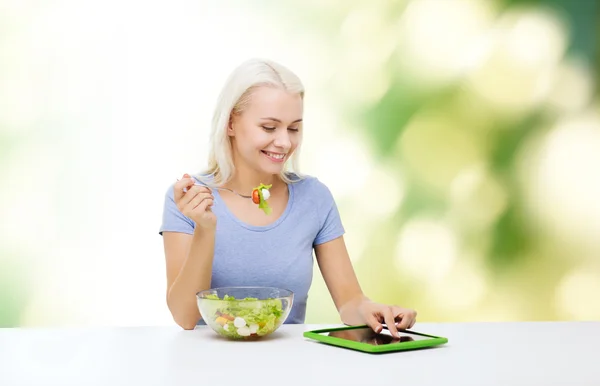 Smilende kvinne som spiser salat med nettbrett – stockfoto