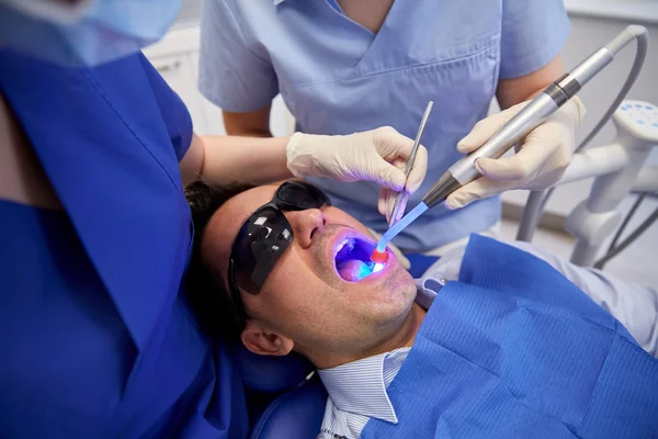 Dentistas que tratan dientes masculinos de pacientes en la clínica —  Fotos de Stock