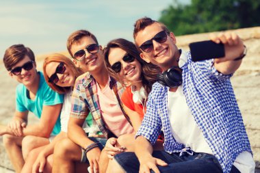 group of smiling friends with smartphone outdoors clipart