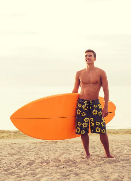 Lächelnder junger Mann mit Surfbrett am Strand — Stockfoto