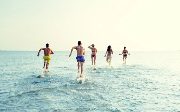 Amis souriants courir sur la plage de dos — Photo