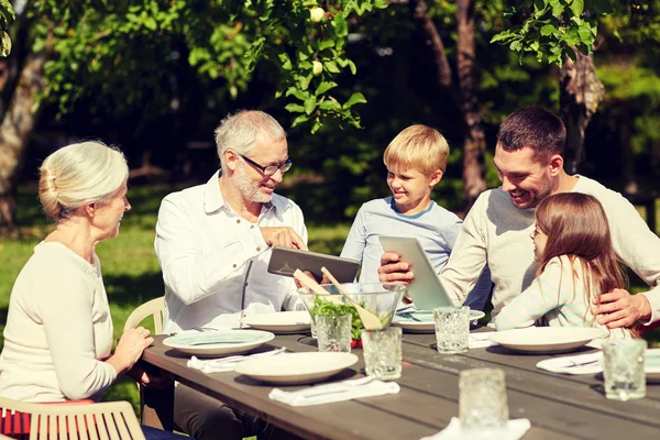 Happy family with tablet pc at table in garden — Stock Photo, Image