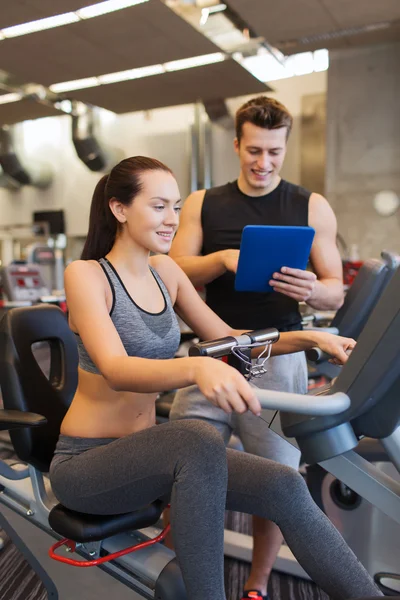 Glad kvinna med tränare på motionscykel i gym — Stockfoto