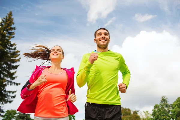 Sonriente pareja con auriculares corriendo al aire libre — Foto de Stock