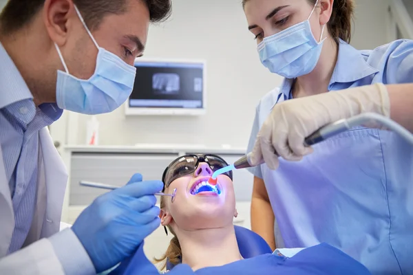 Dentistas que tratan dientes de paciente mujer en la clínica —  Fotos de Stock