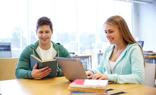 Estudiantes felices con portátil y libros en la biblioteca — Foto de Stock