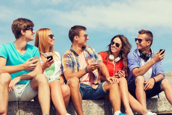 Grupo de amigos sonrientes con teléfonos inteligentes al aire libre —  Fotos de Stock