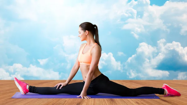 Smiling woman doing splits on mat over clouds — Stockfoto