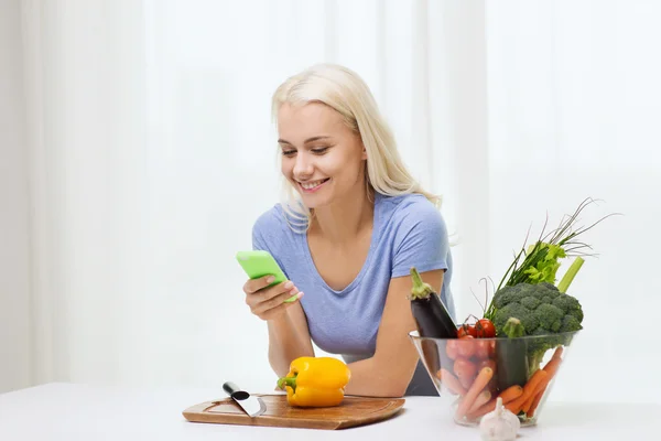 Smiling woman with smartphone cooking vegetables — Stock Photo, Image