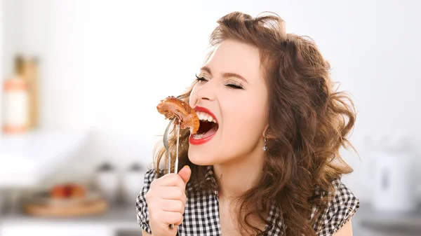 Jovem faminto comendo carne em garfo na cozinha Imagens Royalty-Free