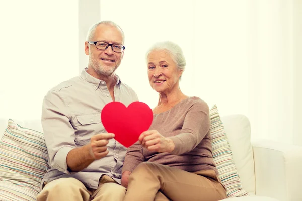 Happy senior couple with red heart shape at home — Stock Photo, Image