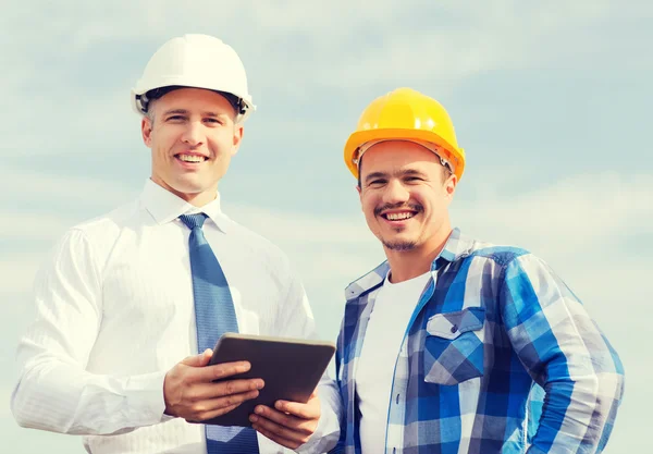 Construtores sorridentes em hardhats com tablet pc — Fotografia de Stock