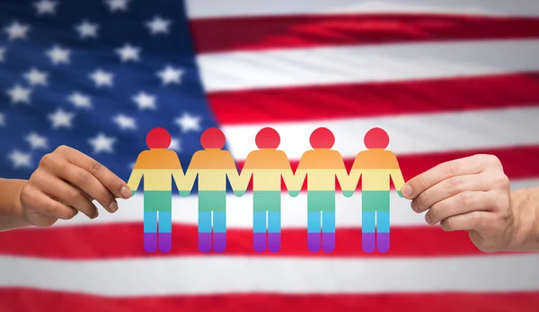 Manos sosteniendo a la gente del arco iris sobre la bandera americana — Foto de Stock