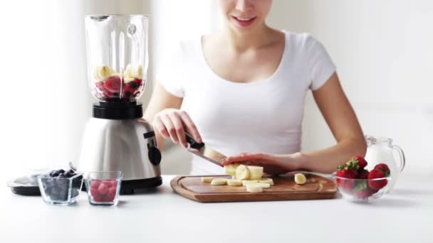 Lächelnde junge Frau mit Mixer, der Bananen schneidet — Stockvideo