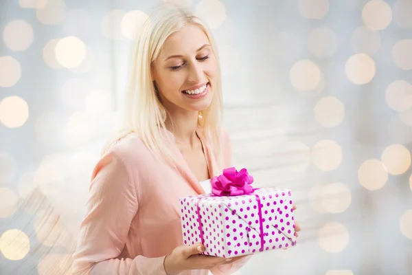 Mujer sonriente con caja de regalo sobre luces navideñas — Foto de Stock