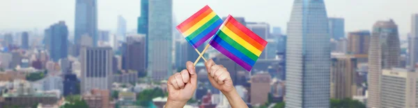 Hands holding rainbow flags over city background — Stok fotoğraf
