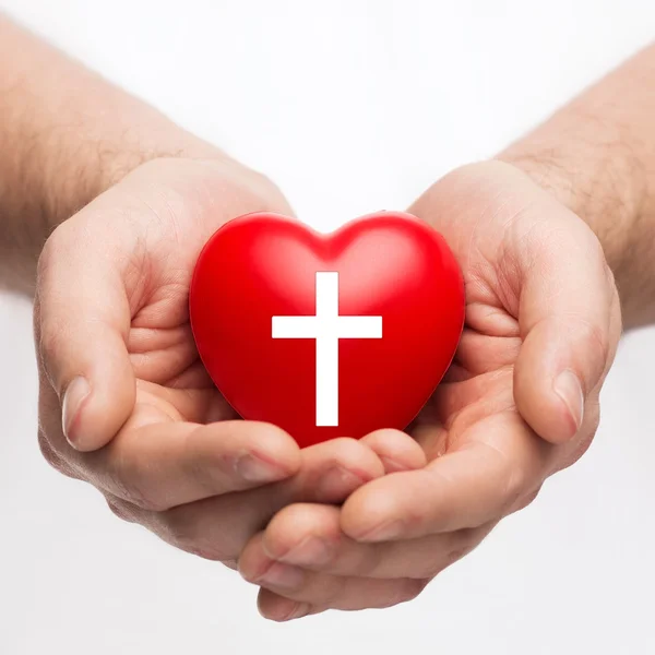 Mãos masculinas segurando coração com símbolo de cruz — Fotografia de Stock