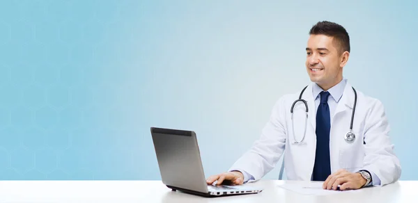 Усміхнений чоловік лікар з ноутбуком сидить за столом — стокове фото