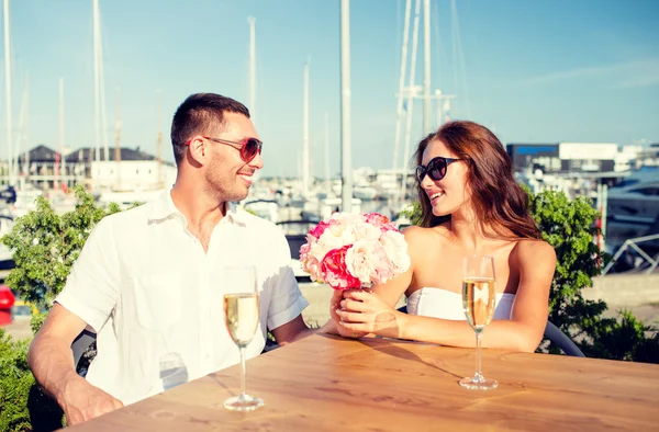 Smiling couple with bunch and champagne at cafe — Stock Photo, Image