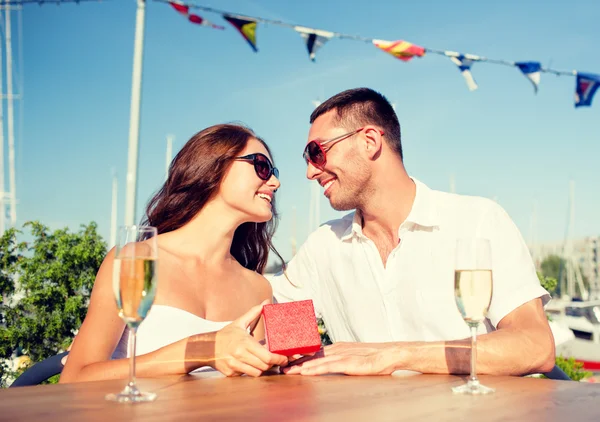 Lächelndes Paar mit Champagner und Geschenk im Café — Stockfoto