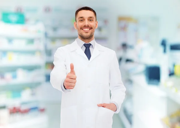 Улыбающийся фармацевт, показывающий большие пальцы в аптеке — стоковое фото