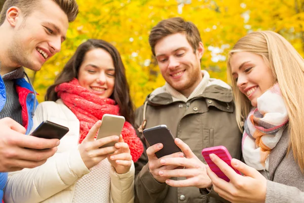 Amici sorridenti con smartphone nel parco autunnale — Foto Stock