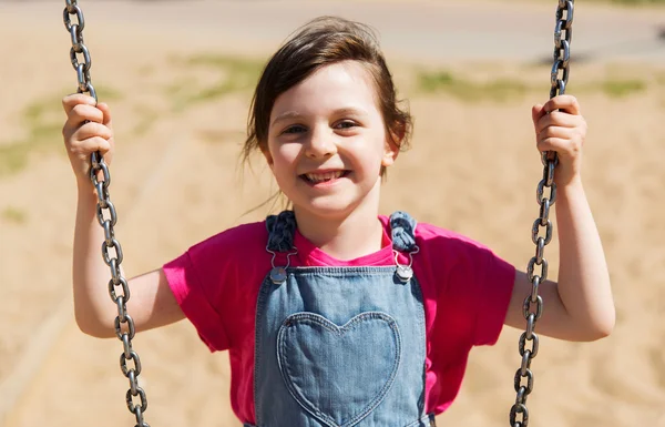 Fröhliches kleines Mädchen schaukelt auf Schaukel auf Spielplatz — Stockfoto