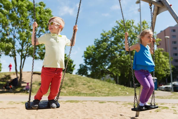 Dos niños felices balanceándose en el columpio en el patio de juegos —  Fotos de Stock