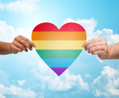 human hands with rainbow heart shape over blue sky clipart