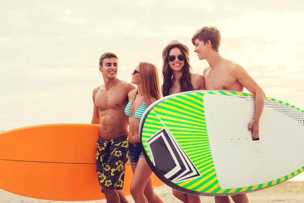 Amigos sonrientes en gafas de sol con surfos en la playa — Foto de Stock