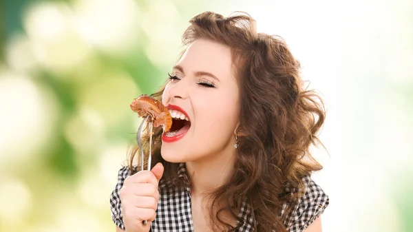 Hungry young woman eating meat on fork over green — Stockfoto