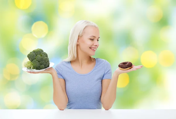 Mujer sonriente con brócoli y donut — Foto de Stock