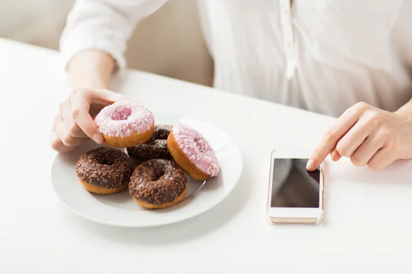 Close up de mãos com telefone inteligente e donuts — Fotografia de Stock