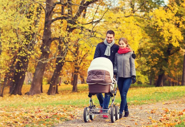 Pareja sonriente con cochecito de bebé en el parque de otoño —  Fotos de Stock